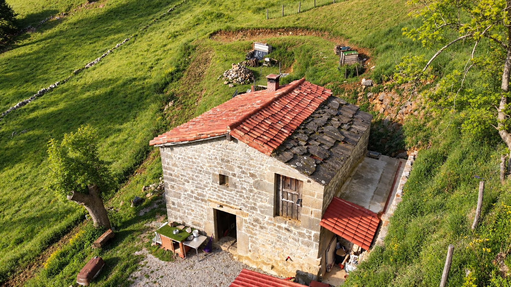 Vista aérea de la cabaña pasiega con tejado de teja roja rodeada de monte verde
